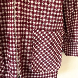 Puede incluir: Primer plano de una chaqueta a cuadros burdeos y blancos con cremallera plateada y bolsillo. El patr&oacute;n de la chaqueta es un dise&ntilde;o cl&aacute;sico de cuadros vichy, con el bolsillo que refleja el mismo patr&oacute;n. El pu&ntilde;o de la manga es visible.