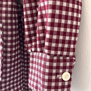 Puede incluir: Primer plano de una tela con estampado de cuadros burdeos y blancos. La tela est&aacute; en una manga con pu&ntilde;o abotonado. El patr&oacute;n es un dise&ntilde;o cl&aacute;sico de cuadros vichy, con peque&ntilde;os cuadrados burdeos y blancos. El pu&ntilde;o tiene un solo bot&oacute;n blanco redondo.