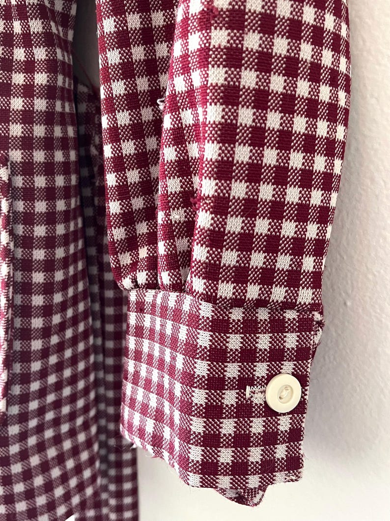 Puede incluir: Primer plano de una tela con estampado de cuadros burdeos y blancos. La tela est&aacute; en una manga con pu&ntilde;o abotonado. El patr&oacute;n es un dise&ntilde;o cl&aacute;sico de cuadros vichy, con peque&ntilde;os cuadrados burdeos y blancos. El pu&ntilde;o tiene un solo bot&oacute;n blanco redondo.