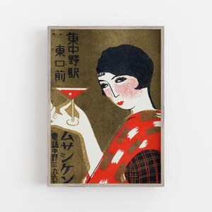 K&ouml;nnte beinhalten: Vintage japanischer Kunstdruck mit einer Frau, die einen Cocktail h&auml;lt. Das Kunstwerk hat einen goldenen Hintergrund mit japanischem Text und eine Frau in einem rot-schwarz gemusterten Kimono. Die Frau hat schwarzes Haar und roten Lippenstift. Der Cocktail ist rot.