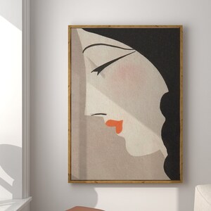 May include: A framed art print featuring a stylized profile of a woman with closed eyes, red lips, and black hair. The artwork is set against a neutral background and framed in a gold-colored frame. The art hangs on a white wall.