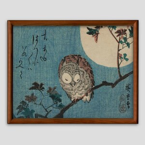 May include: A woodblock print of an owl perched on a branch with a full moon in the background. The owl is brown and gray with large, dark eyes. The branch is bare except for a few leaves. The moon is white and surrounded by a blue sky. The print is signed in Japanese characters.