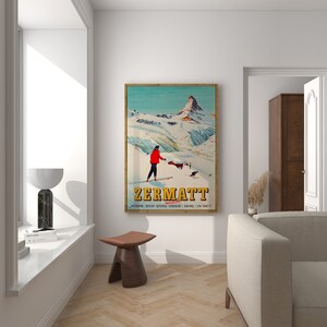 Puede incluir: Un cartel de viaje vintage para Zermatt, Suiza, con un esquiador con ropa roja sobre un fondo de monta&ntilde;a nevado. El cartel tiene un esquema de color azul, verde y blanco e incluye el texto "Zermatt, Suiza".
