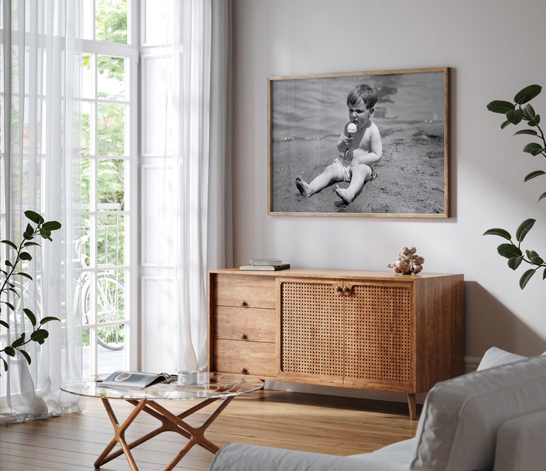 May include: A wooden cabinet with a woven rattan door and three drawers. The cabinet is in a living room with a white couch, a glass coffee table, and a black and white photo of a child on the beach.