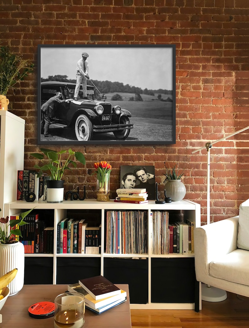 Op de afbeelding: Een zwart-witfoto van twee mannen die naast een vintage auto staan. De man links houdt een golfclub vast en de man rechts staat op de treeplank van de auto. De auto heeft een kentekenplaat met de tekst "DG 567".
