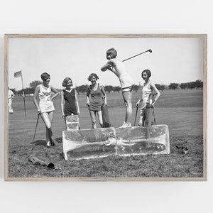 May include: Five women in vintage clothing playing golf on a grassy field. The women are standing on blocks of ice, and one woman is swinging a golf club. The women are wearing short skirts, sleeveless shirts, and hats. The image is in black and white.