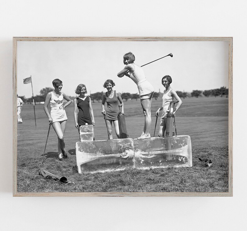 May include: Five women in vintage clothing playing golf on a grassy field. The women are standing on blocks of ice, and one woman is swinging a golf club. The women are wearing short skirts, sleeveless shirts, and hats. The image is in black and white.