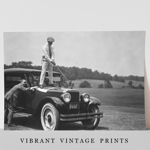 Op de afbeelding: Een zwart-witte vintage foto van twee mannen die golfen. Een man staat op de motorkap van een vintage auto en houdt een golfclub vast, terwijl de andere man op de grond staat en naar hem opkijkt. De auto heeft een kentekenplaat met de tekst "DG-567".
