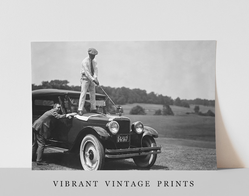 Op de afbeelding: Een zwart-witte vintage foto van twee mannen die golfen. Een man staat op de motorkap van een vintage auto en houdt een golfclub vast, terwijl de andere man op de grond staat en naar hem opkijkt. De auto heeft een kentekenplaat met de tekst "DG-567".