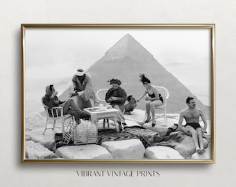 Könnte beinhalten: Ein Schwarzweißfoto einer Gruppe von Menschen, die ein Picknick auf einer großen Pyramide veranstalten. Die Menschen sitzen auf Felsen und in Stühlen, und es gibt einen Tisch mit Essen und Getränken. Die Pyramide ist im Hintergrund, und der Himmel ist bewölkt.
