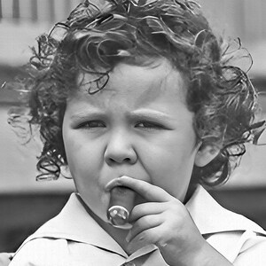 Peut inclure: Un jeune enfant aux cheveux boucl&eacute;s tient un cigare dans sa main et regarde la cam&eacute;ra.