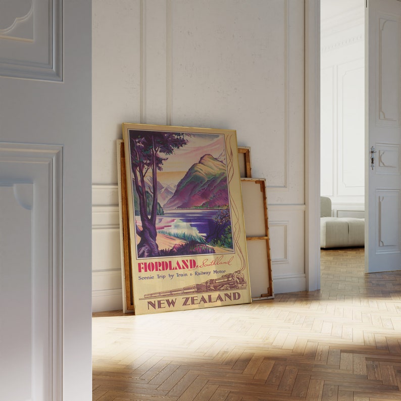 Puede incluir: Un p&oacute;ster de viaje vintage de Fiordland, Nueva Zelanda, que presenta un paisaje esc&eacute;nico con monta&ntilde;as, un lago y un tren. El p&oacute;ster tiene un marco dorado y est&aacute; apoyado contra una pared blanca. El texto dice "Fiordland, Southland" y "Scenic Trip by Train & Railway Motor."