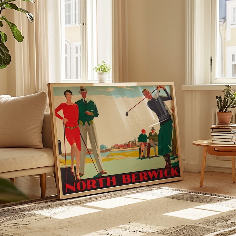 May include: A framed vintage-style poster with the text "NORTH BERWICK" in red. The poster depicts a golf scene with figures in period attire, including a woman in a red dress and a man in a green jacket. The frame is a light wood color.