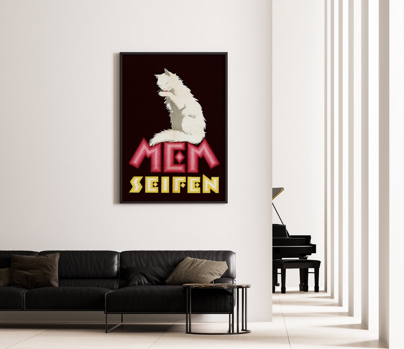 May include: A framed poster featuring a white cat grooming itself. The poster has a dark background with the words "MEM SEIFEN" in red and yellow stylized text. The poster is hanging on a white wall above a black leather sofa.