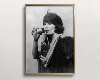 Könnte beinhalten: Ein Schwarzweißfoto einer Frau, die einen Turban und einen langen Mantel trägt, ein kleines Buch hält und eine Pfeife raucht.