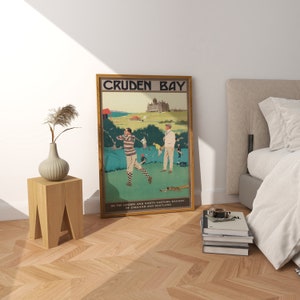 May include: A vintage travel poster advertising Cruden Bay, a golf course in Scotland. The poster features two golfers on a green course with a large building in the background. The text on the poster reads "Cruden Bay" and "On the London and North Eastern Railway of England and Scotland."