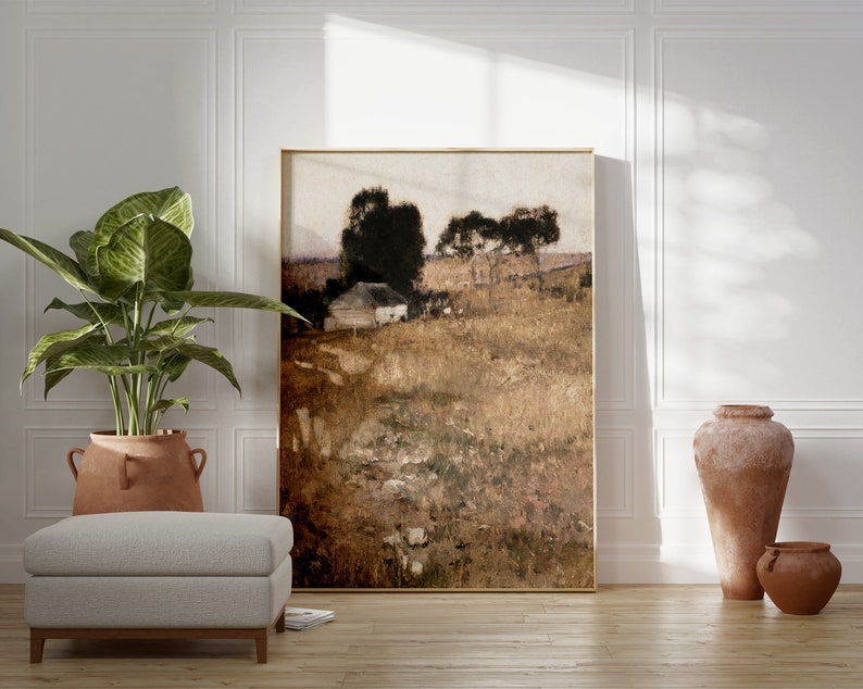 May include: A framed landscape painting of a rural scene with a small house, trees, and a field. The painting is in a light brown frame and is hanging on a white wall. There are two terracotta pots on the floor in front of the painting.
