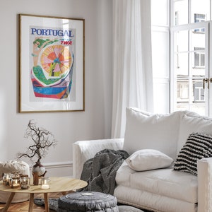 May include: A white couch with black and white striped throw blanket and pillows in a living room with a wooden floor. A framed poster with the text "PORTUGAL FLY TWA" hangs on the wall. A small table with a vase and candles sits in front of the couch.