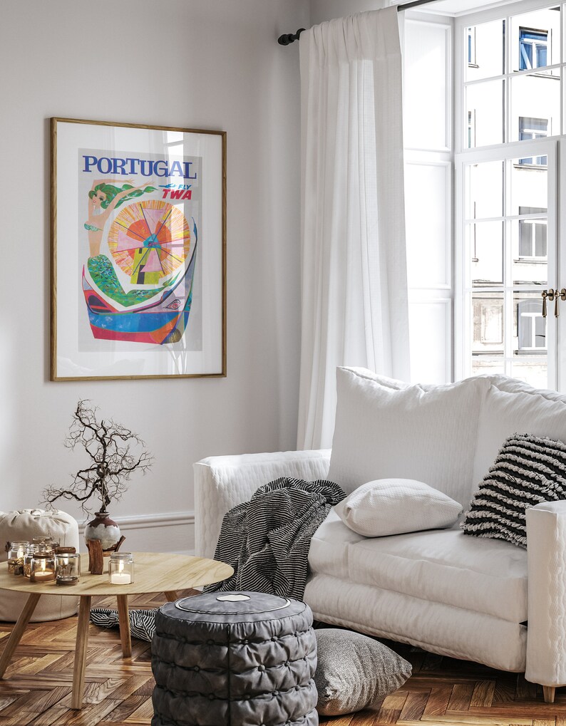 May include: A white couch with black and white striped throw blanket and pillows in a living room with a wooden floor. A framed poster with the text "PORTUGAL FLY TWA" hangs on the wall. A small table with a vase and candles sits in front of the couch.