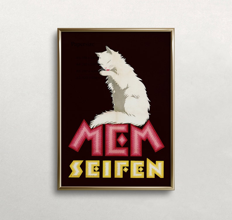 May include: Framed vintage advertisement featuring a white cat grooming itself. The cat sits atop the word "MEM" in pink, with "SEIFEN" in yellow below. The background is dark brown, and the frame is gold.