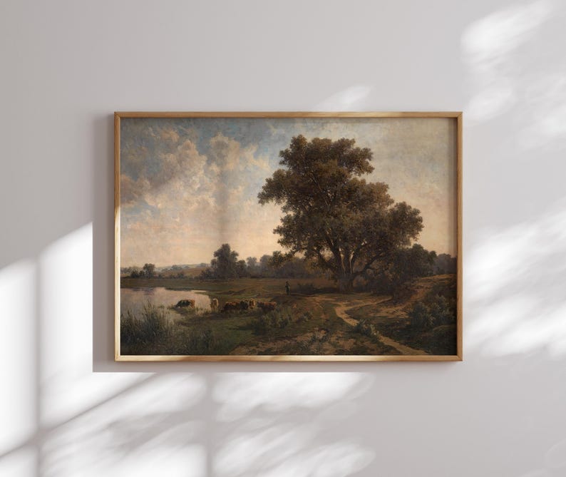 K&ouml;nnte beinhalten: Ein gerahmtes Landschaftsgem&auml;lde, das eine l&auml;ndliche Szene mit einem gro&szlig;en Baum im Vordergrund, einem Fluss und einer Gruppe von Rindern in der Ferne zeigt. Der Himmel ist hellblau mit flauschigen wei&szlig;en Wolken.