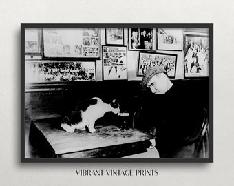 May include: Black and white photograph of a man wearing a cap sitting at a desk with a black and white cat. The man is looking down at the cat. The photo is surrounded by smaller black and white photos of people and sports teams.
