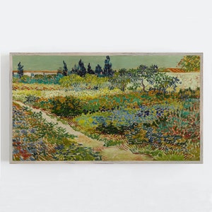May include: A framed print depicting a garden scene with a path winding through colourful flowers and plants. The artwork uses greens, blues, yellows, and reds, with a light blue sky and a white wall. The frame is a light wood colour.