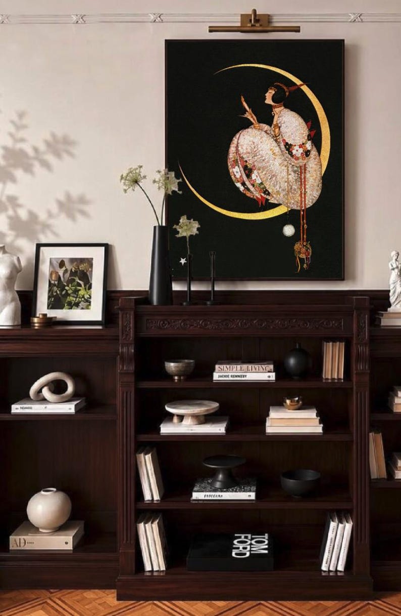 Op de afbeelding: Een donkerhouten boekenplank met meerdere planken gevuld met boeken, decoratieve schalen en sokkels. Boven de plank hangt een ingelijste kunstdruk met een figuur in een kledingstuk met patronen, zittend in een gouden halve maan op zwart.