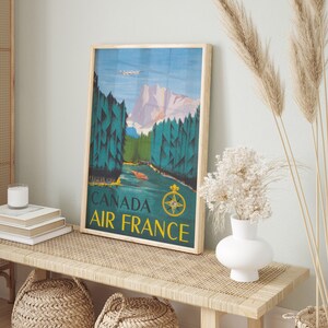 May include: A vintage travel poster with a blue, green, and brown color scheme. The poster features a mountain range, a river, and a plane flying overhead. The text on the poster reads "Canada Air France".