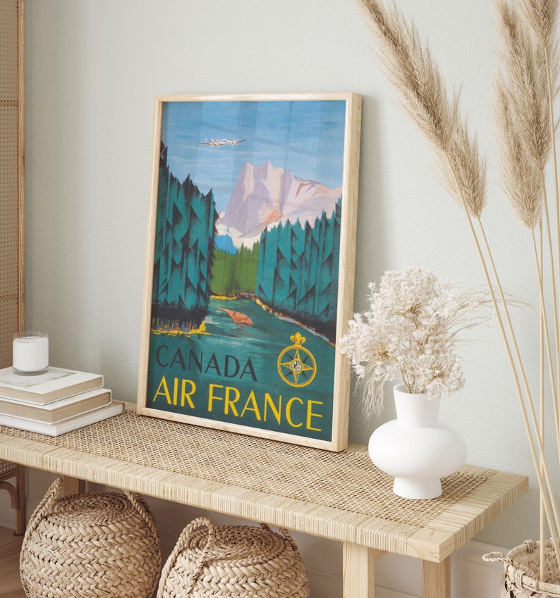 May include: A vintage travel poster with a blue, green, and brown color scheme. The poster features a mountain range, a river, and a plane flying overhead. The text on the poster reads "Canada Air France".
