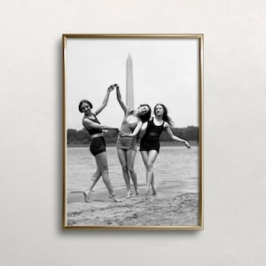 May include: A framed black and white photograph of three people in vintage swimwear dancing on a beach. The Washington Monument is visible in the background. The photograph is in a gold frame.
