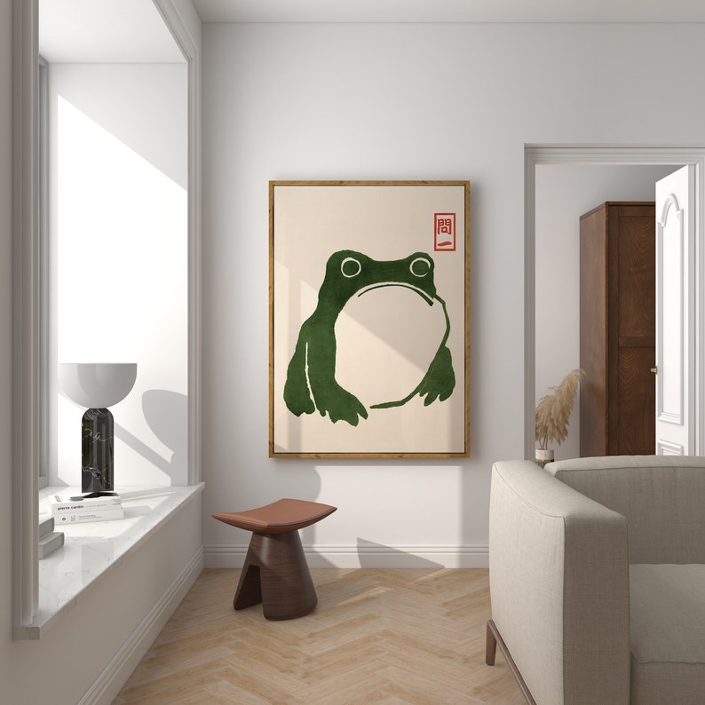 May include: A framed print of a green frog with a white background. The frog is facing forward with its mouth closed. The print has a red square with the Japanese character "開" in the top right corner.