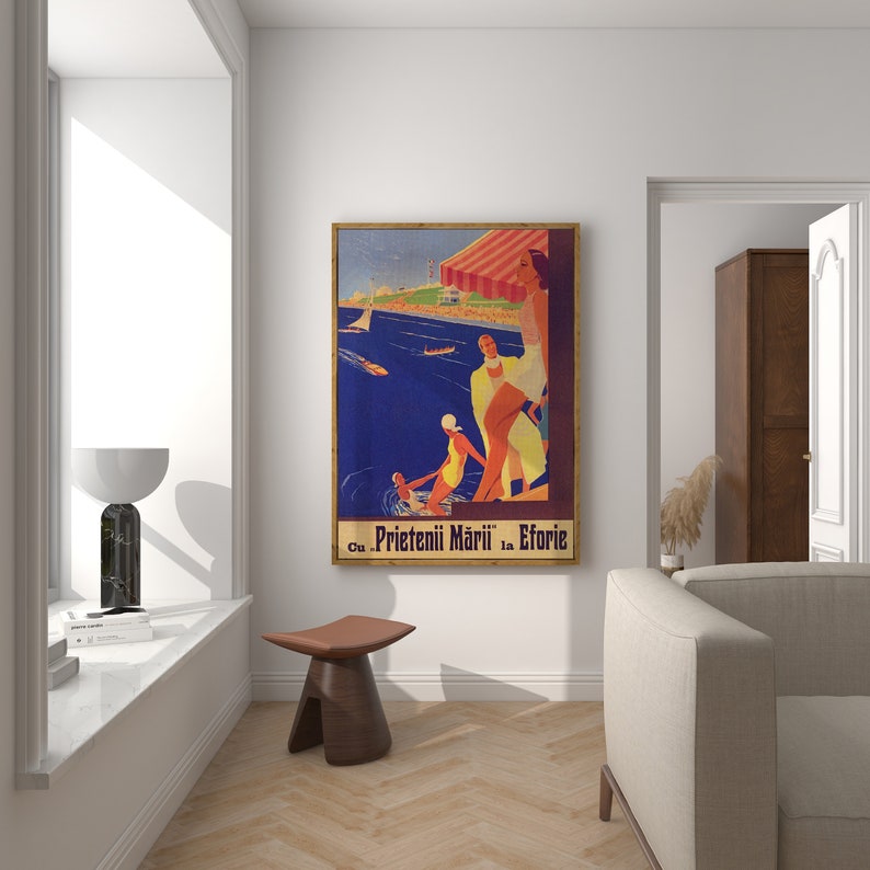 May include: A framed vintage travel poster with a beach scene. The poster features figures in swimwear, boats on the water, and the text "Cu Prietenii Mării la Eforie". The poster has a wooden frame and is displayed in a well-lit room.