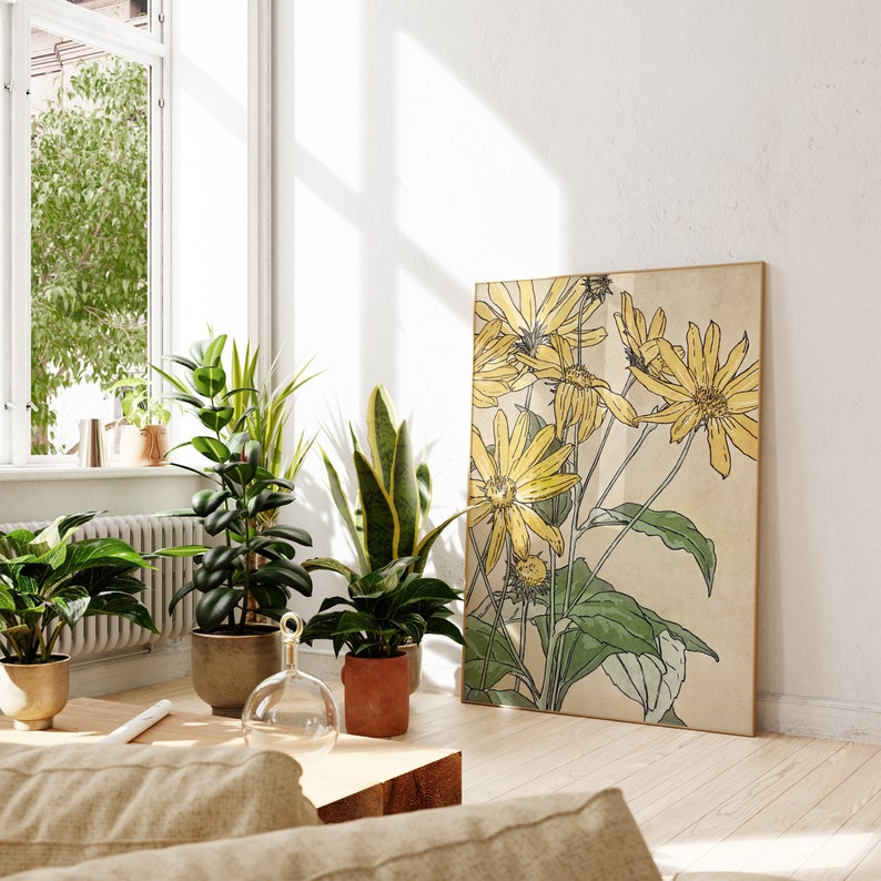 May include: A botanical illustration of yellow flowers with green leaves on a beige background. The print is framed and hanging on a white wall in a room with plants and a window.
