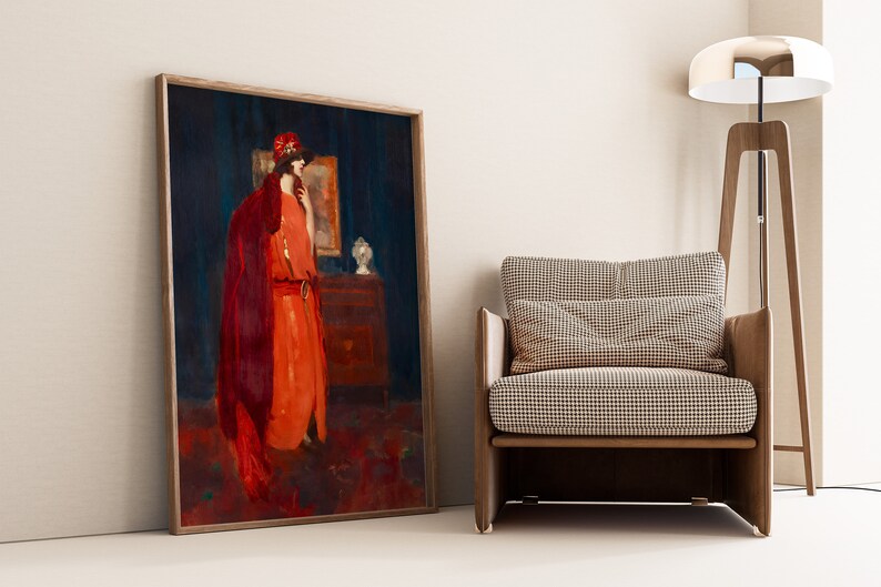 May include: A framed painting of a woman in a red dress and a red hat standing in a room with a dark blue wall. The woman is looking to the side and holding a small object in her hand. There is a dresser with a lamp on it in the background.