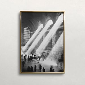 以下が含まれることがあります： 窓から差し込む太陽光が、下の人々を照らしている、壮大な駅舎の内部を捉えた白黒写真です。