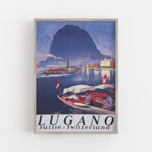 May include: A framed vintage travel poster for Lugano, Switzerland. The poster depicts a lake scene with boats and a mountain. The text "LUGANO Suisse / Switzerland" is at the bottom.