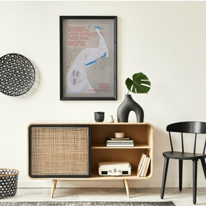 Op de afbeelding: Een modern interieur met een licht houten kast met een geweven deur, een zwarte stoel en een ingelijste poster. Een zwarte vaas bevat een groen blad. Decoratieve zwarte wandkunst en een mand zijn ook aanwezig.