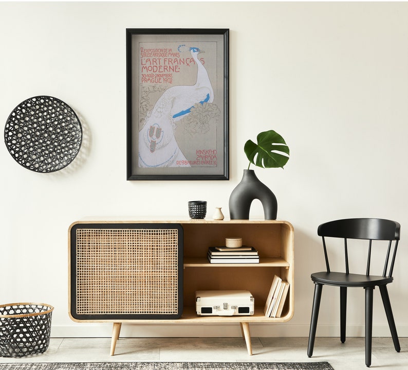 Op de afbeelding: Een modern interieur met een licht houten kast met een geweven deur, een zwarte stoel en een ingelijste poster. Een zwarte vaas bevat een groen blad. Decoratieve zwarte wandkunst en een mand zijn ook aanwezig.