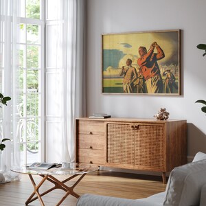Pu&ograve; includere: Un soggiorno in stile moderno di met&agrave; secolo con un mobile in legno con una porta in rattan intrecciato. Il mobile &egrave; decorato con una stampa vintage incorniciata di tre uomini che giocano a golf. La stanza presenta anche un tavolino da caff&egrave; in vetro e un divano bianco.