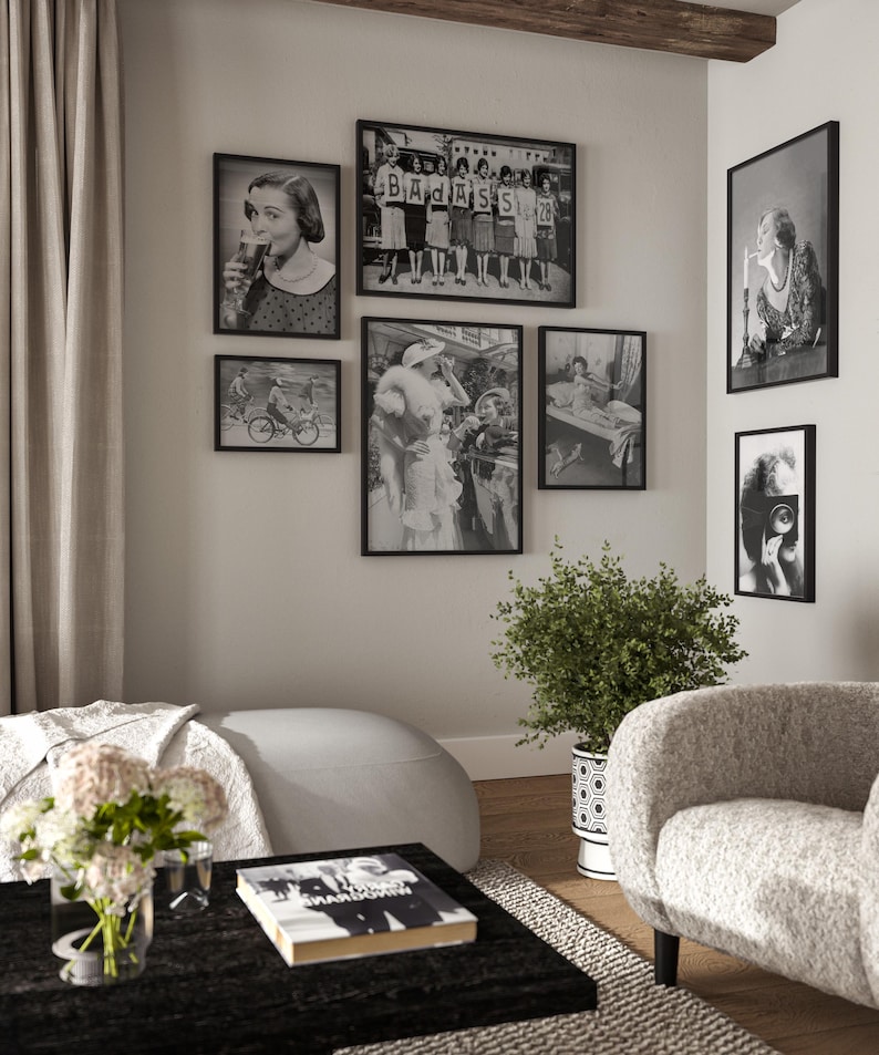 May include: A living room interior with a white sofa, a black coffee table, and a white armchair. The wall is decorated with black framed photographs in various sizes. The photographs are black and white and feature people and scenes from the past. A potted plant sits on the floor next to the armchair.