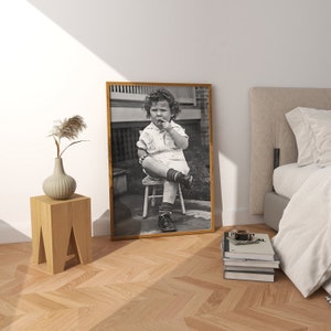 Peut inclure: Photographie en noir et blanc d'un jeune enfant assis sur un petit tabouret en bois. L'enfant porte une chemise blanche et un pantalon fonc&eacute;. La photo est encadr&eacute;e dans un cadre en bois.