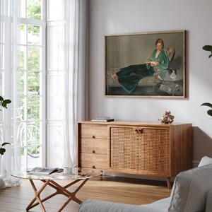 May include: A wooden cabinet with a woven rattan door and three drawers. The cabinet is in a living room with a painting of a woman in a green dress on the wall behind it.