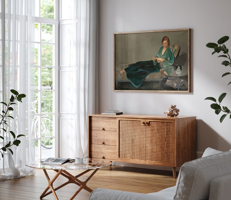 May include: A wooden cabinet with a woven rattan door and three drawers. The cabinet is in a living room with a painting of a woman in a green dress on the wall behind it.