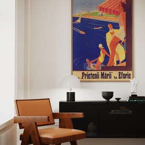 May include: A mid-century modern chair with a brown wooden frame and a tan leather seat. A vintage travel poster in a wooden frame hangs on the wall. The poster features a beach scene with people and the text "Prietenii Mării la Eforie".