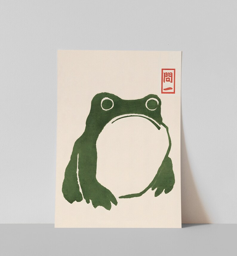 May include: A green frog illustration with a simple, minimalist style. The frog is facing forward with its mouth closed and its eyes wide open. The illustration is on a cream-colored background with a red stamp that says "関".