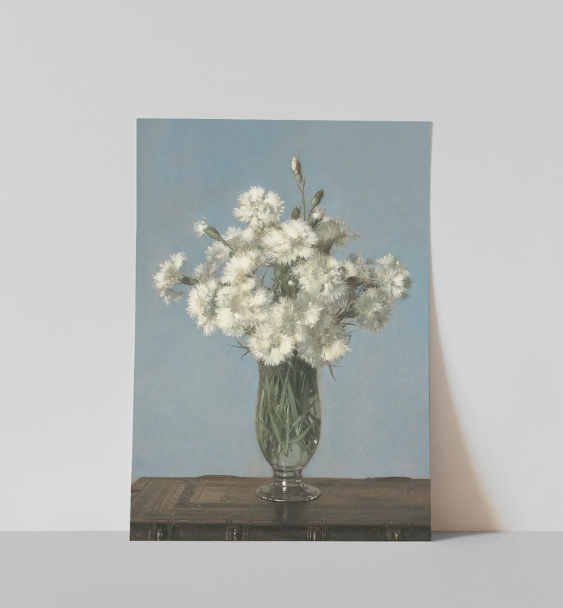 以下が含まれることがあります： 透明なガラスの花瓶に入った白い花の絵。花は密集しており、いくつかのつぼみが見えます。花瓶は、明るい青色の背景に対して、暗い木製の表面に置かれています。