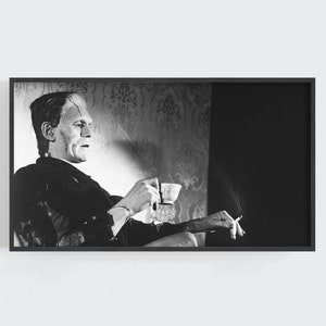 Pode incluir: Uma fotografia a preto e branco de um homem sentado numa cadeira, segurando uma chávena e um cigarro. Ele está a usar um fato e tem uma expressão séria no rosto.
