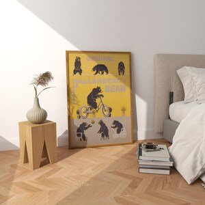 Op de afbeelding: Een ingelijste poster met een gele achtergrond en de tekst "Original Ballenberg Bear". De poster toont illustraties van zwarte beren, waaronder een die op een fiets rijdt. De lijst is lichtbruin en de poster leunt tegen een witte muur.