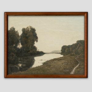 May include: A framed landscape painting depicting a river winding through a forested area. The artwork features muted tones of green, brown, and gray, with trees lining the riverbanks and a path along the shore. The frame is a dark wood.